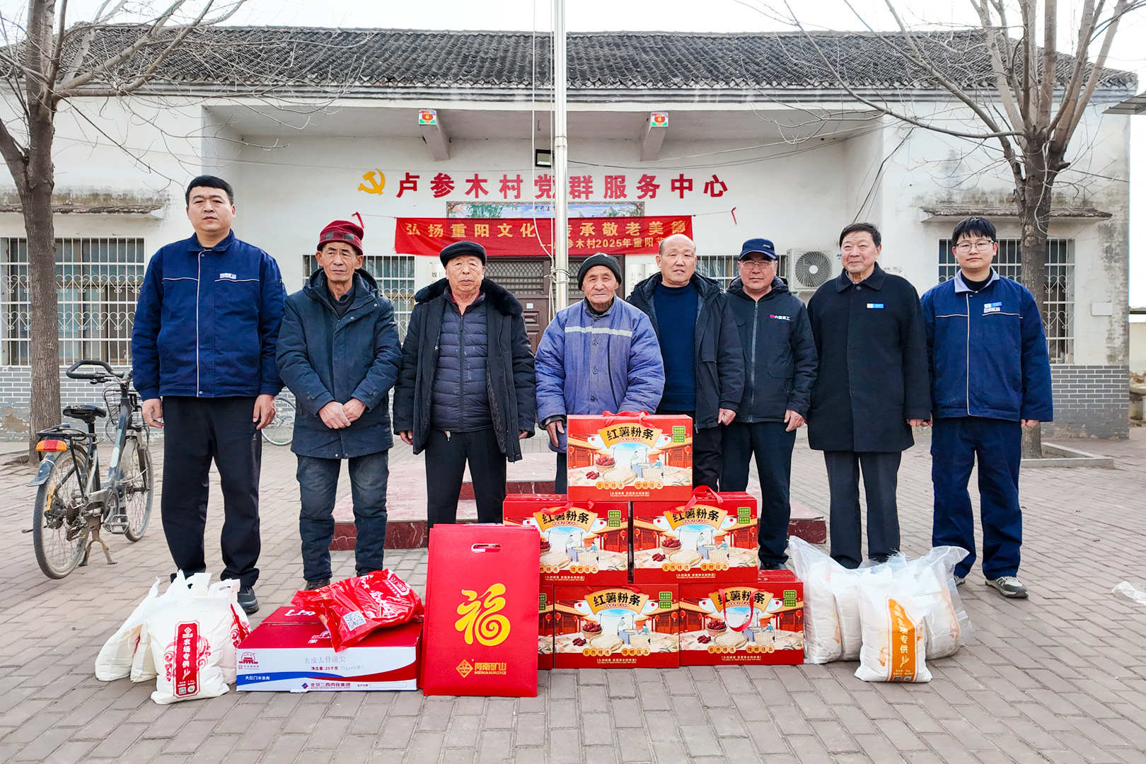 Company representatives and residents with New Year gifts outside a village service building during Henan Mine Crane’s New Year outreach